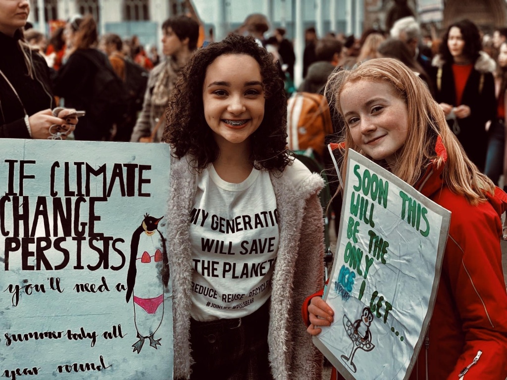 An image of Elena and her friend at the Fridays for Future strike holding banners reading "If climate change persists you'll need a summer body all year round"